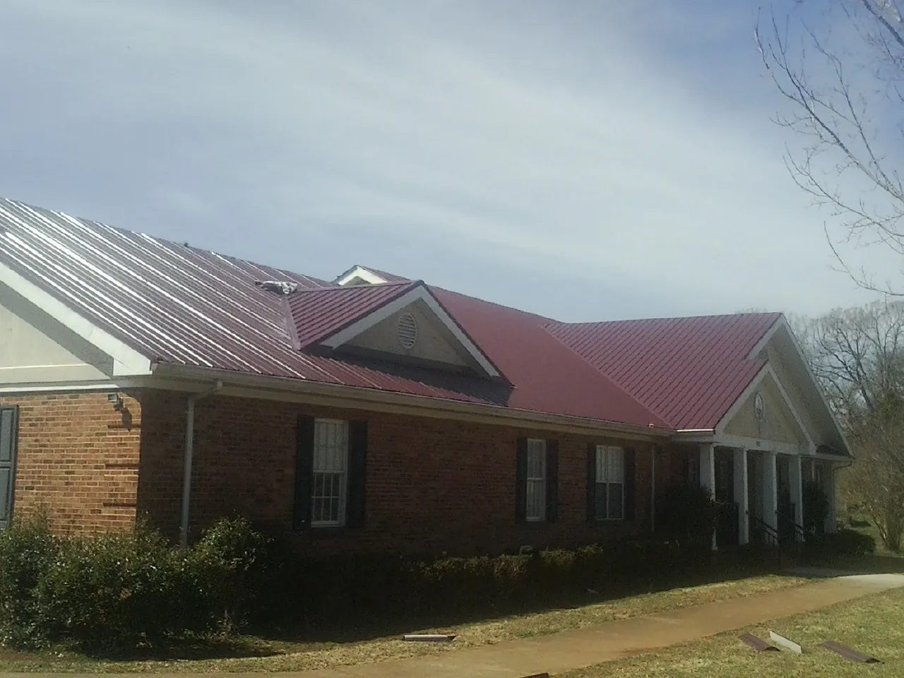 Red metal roof with gabled entries on a long brick building, from a Hail Damage Roof Repair job in Wilson